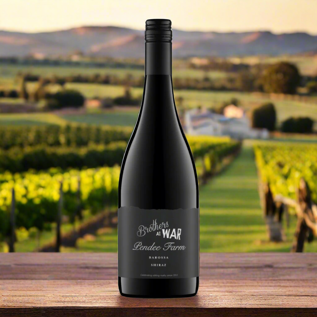 Place a bottle of Brothers at War Pendee Farm Shiraz on a rustic wooden table with a backdrop of Barossa Valley vineyards, gnarled vines, and a vintage farmhouse.