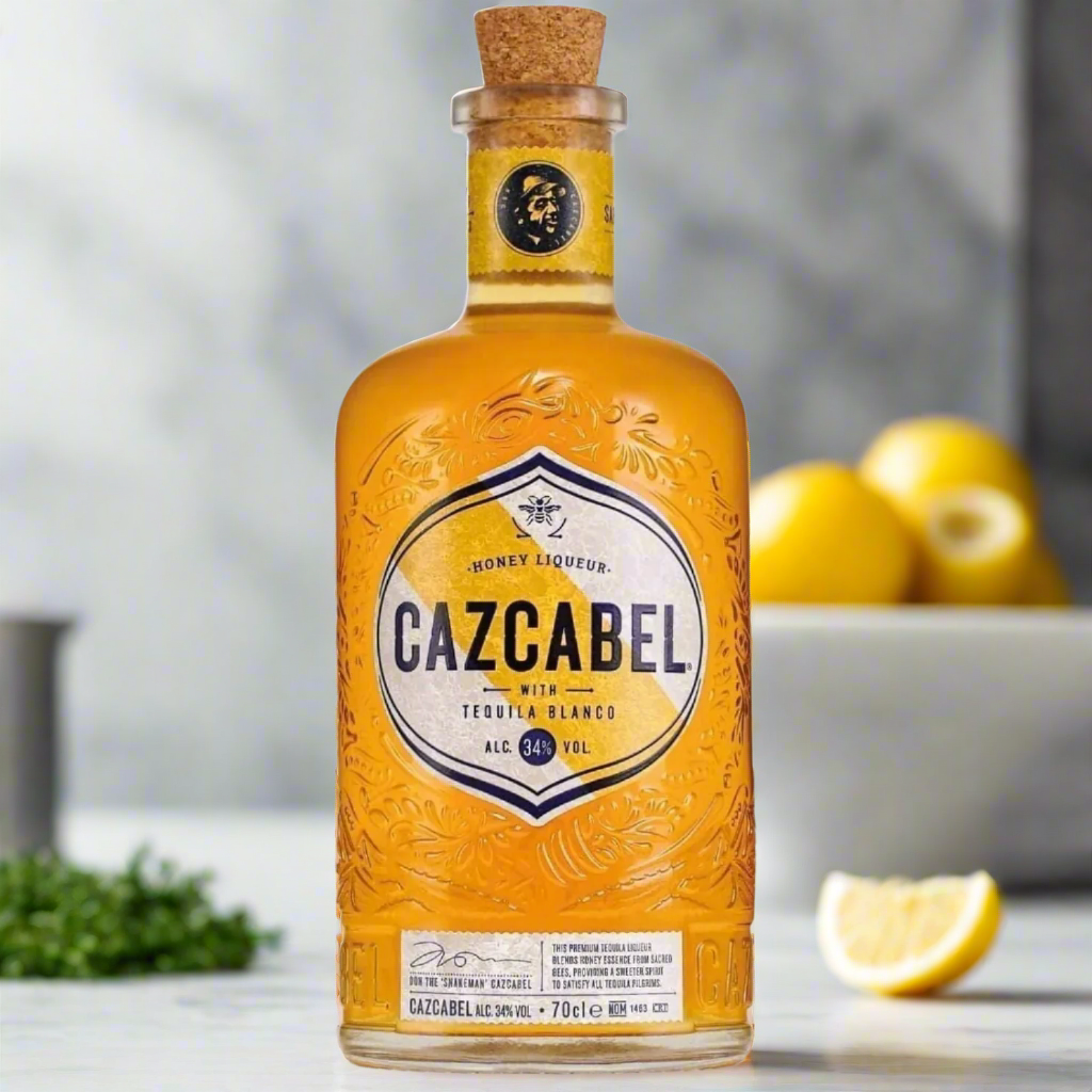 Bottle of Cazcabel honey liqueur with a blurred background of lemons and greenery.