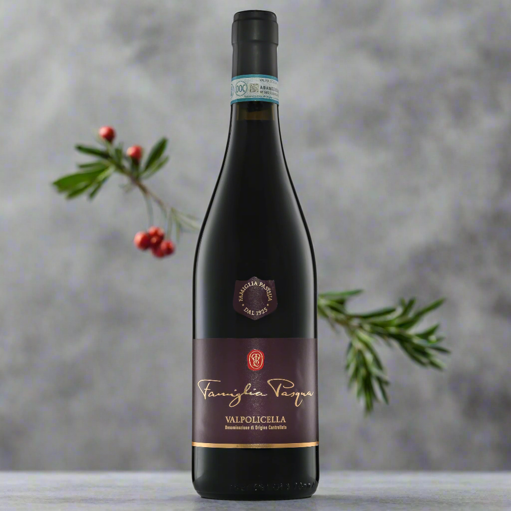 “Famiglia Pasqua Valpolicella DOC bottle on a smooth grey surface with red berries and rosemary sprigs. Clean, minimal background with soft, diffused lighting.”