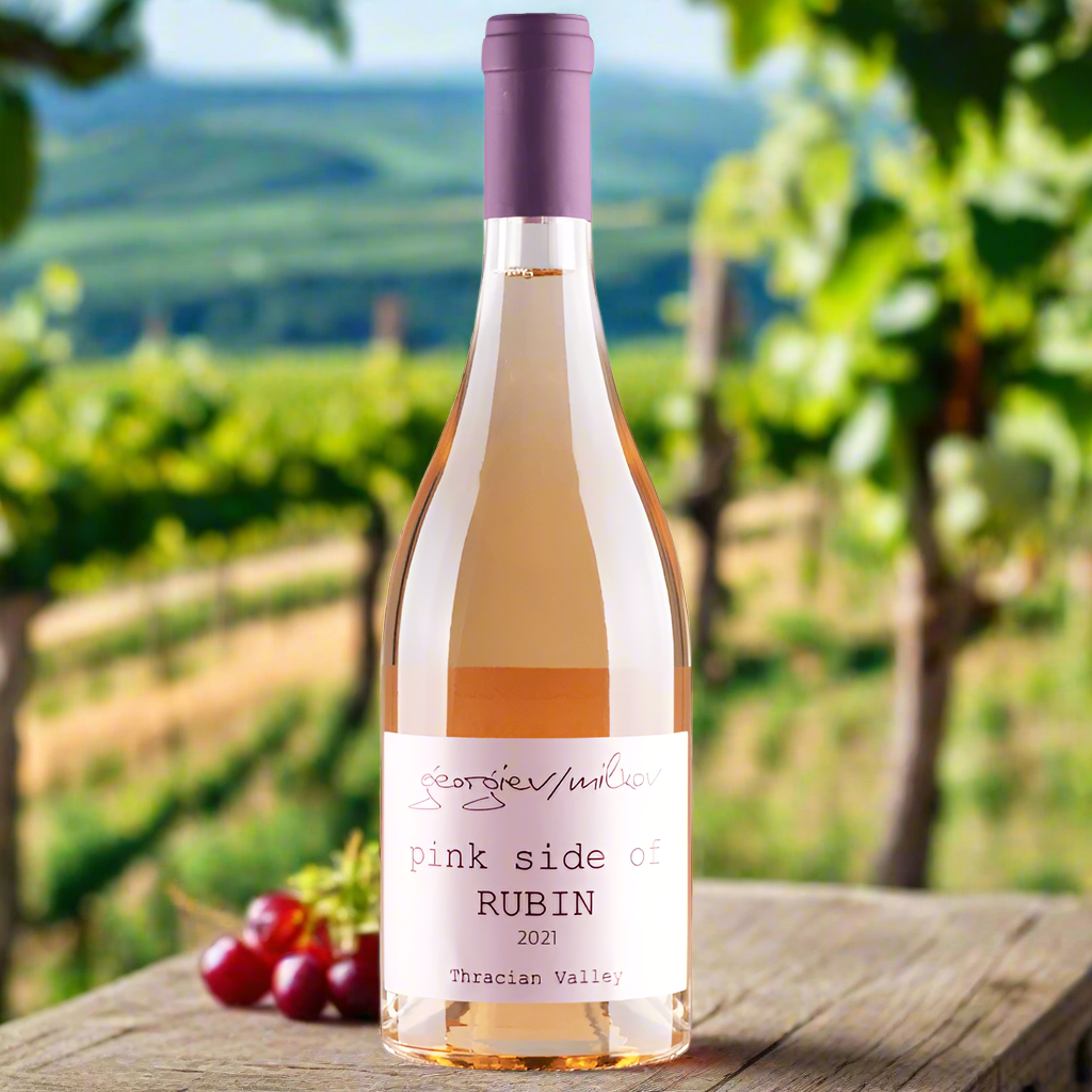 Bottle of 'Pink Side of Rubin' wine with grapes on a wooden table in a vineyard setting