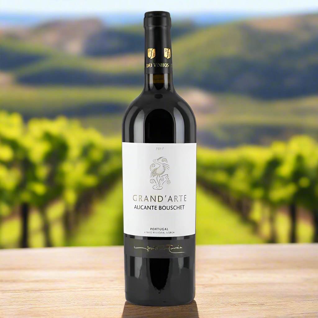 Bottle of Grand'Arte Alicante Bouschet wine on a wooden surface with a blurred vineyard background