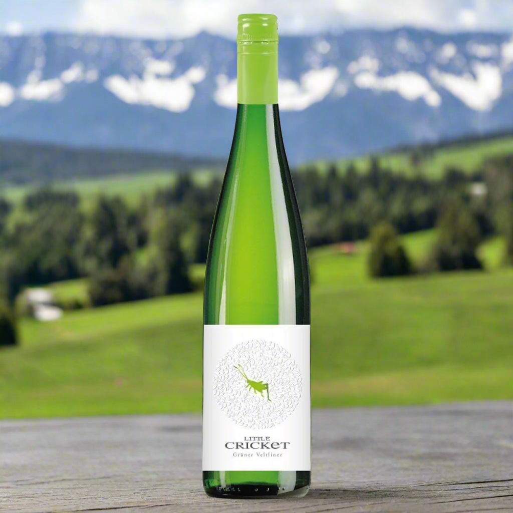 Place a bottle of Little Cricket Grüner Veltliner on a terrace table with views of green alpine hills, clear skies, and distant mountain peaks.
