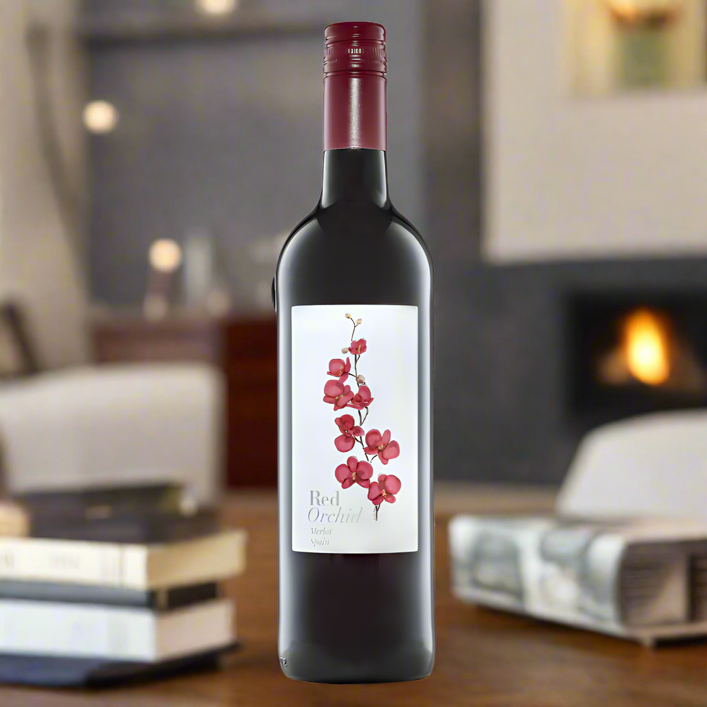 Place a bottle of Red Orchid Merlot on a coffee table in a cozy living room. The background features a warm, inviting space with plush furniture, soft lighting, and a lit fireplace, creating a relaxed and intimate atmosphere perfect for enjoying wine indoors.