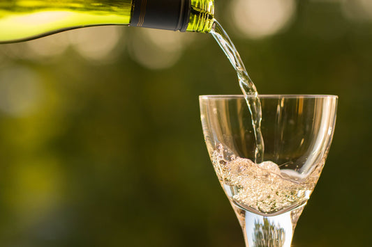 White wine being poured from a bottle against green vineyard backdrop