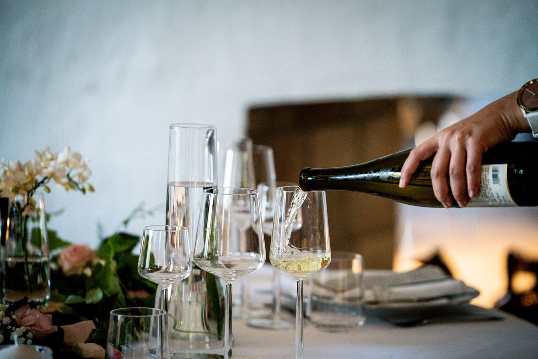 White wine being poured at an elegant dining table set with flowers and glassware