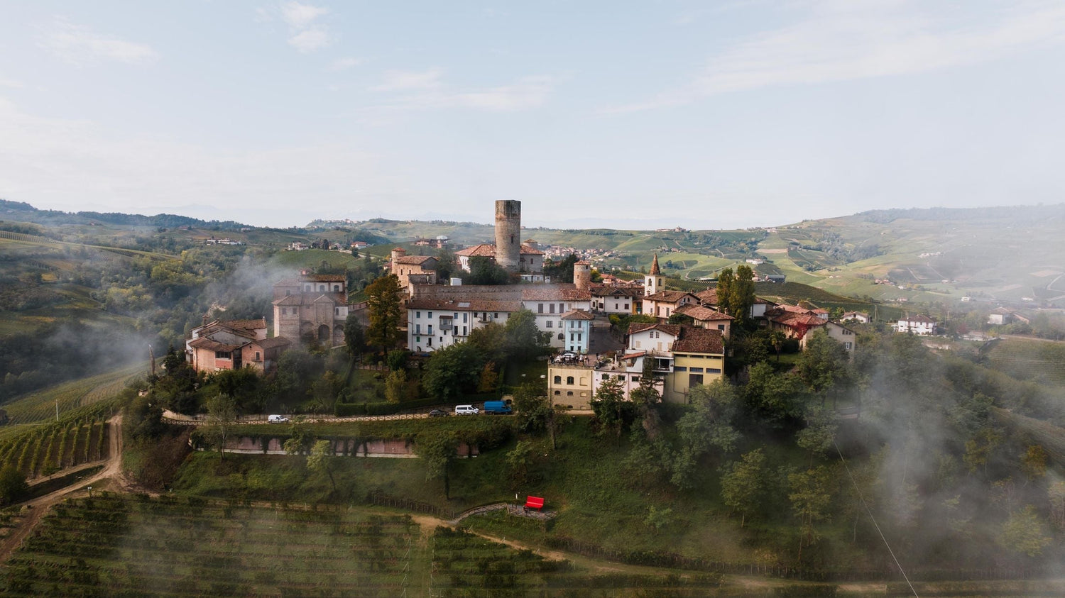 Misty hilltop medieval village with round tower amid rolling vineyard hills, Ca' di Ponti, Piedmont, Italy