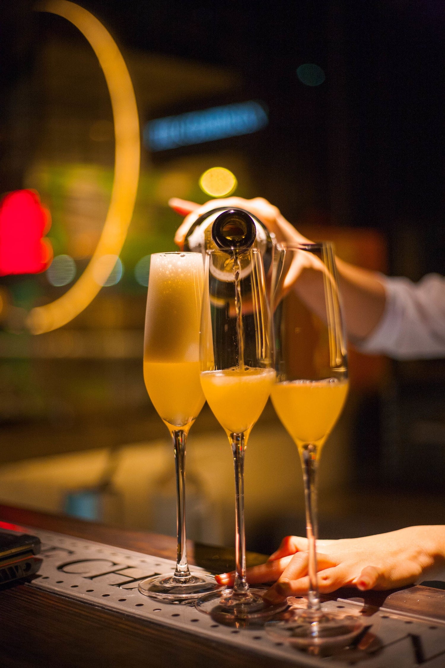 Golden sparkling wine poured into three champagne flutes at a bar with soft bokeh lights, Crémant sparkling wine