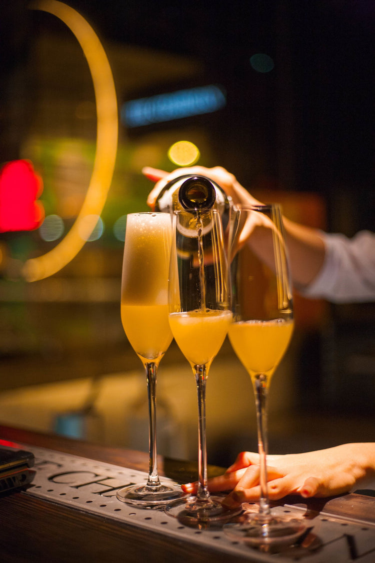 Golden sparkling wine poured into three champagne flutes at a bar with soft bokeh lights, Crémant sparkling wine