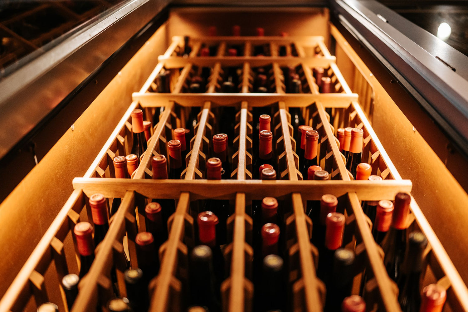 Wine bottles stored horizontally in a wooden wine rack with warm amber lighting, featured wine cases selection