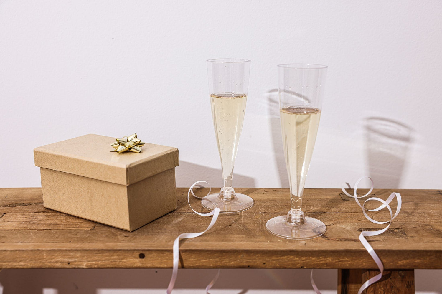 Elegant table setting with champagne flutes, a wrapped gift box and candles for a special wine gift occasion.