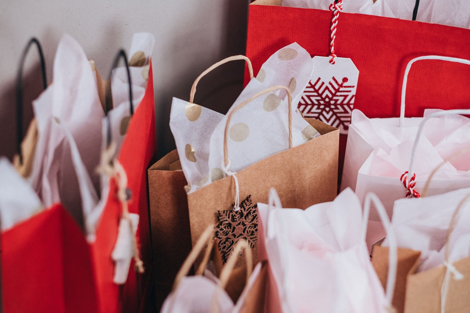 Festive red, kraft and white gift shopping bags filled with tissue paper and holiday gifts — wine gifts under £50.