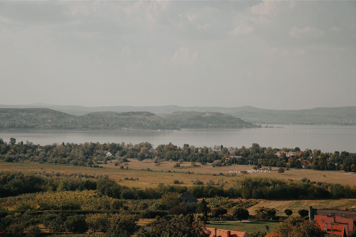 Panoramic view across rolling countryside and a broad lake with wooded hills beyond, Balaton wine region, Hungary.
