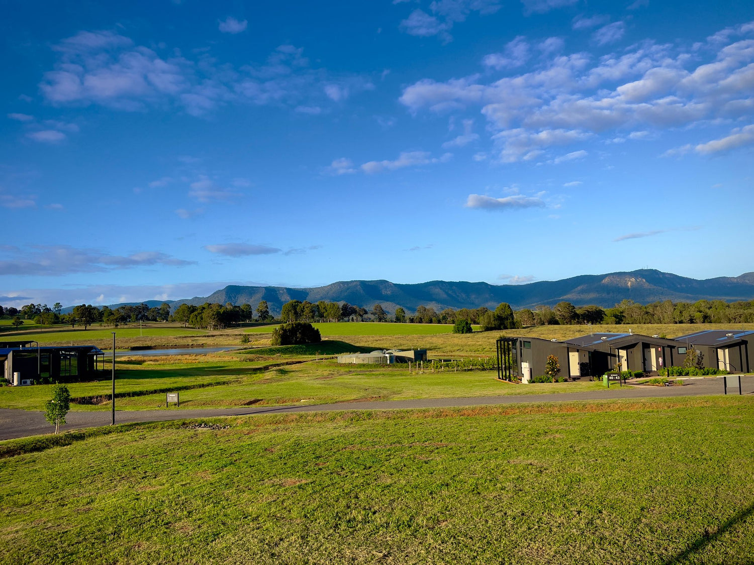 Modern vineyard estate cabins on green lawns with dam ponds and the Hunter Valley mountain ranges behind, New South Wales, Australia.