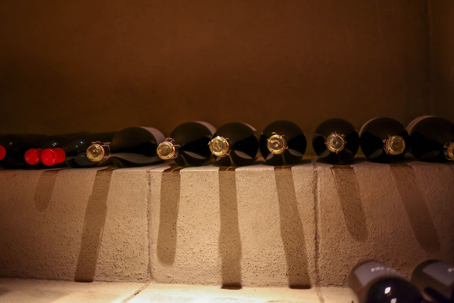 Wine bottles resting cork-end outward in stone cradles in a warm wine cellar, luxury red wines