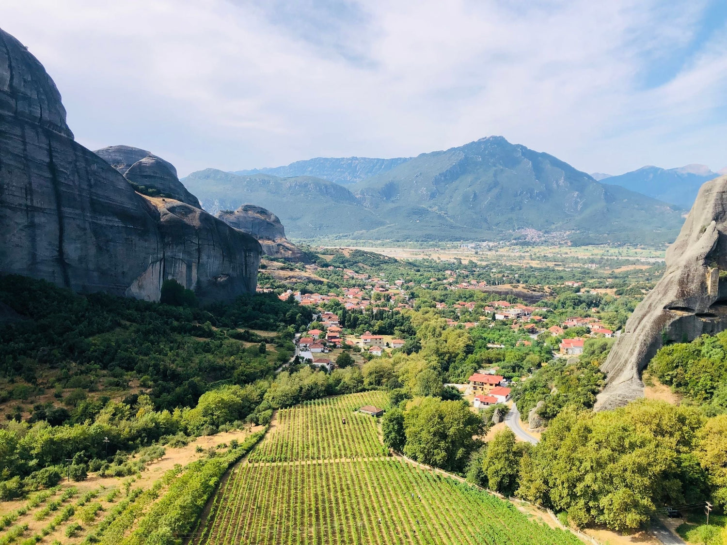 Vineyard below the iconic Meteora rock formations with a Greek village and mountains beyond, northern Greece