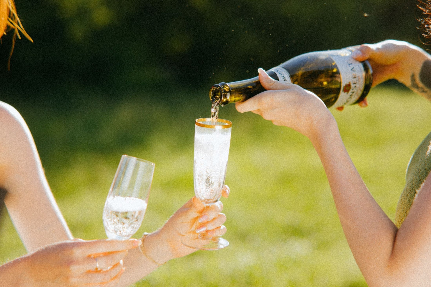 Sparkling wine being poured outdoors into a gold-rimmed champagne flute, celebrating with non-alcoholic sparkling wine