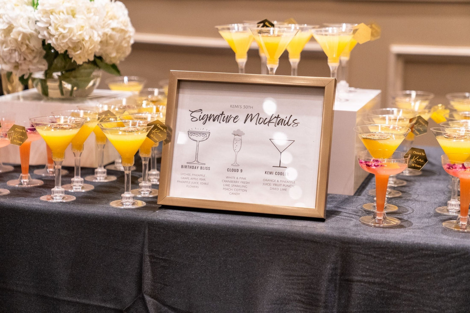 Table of colourful non-alcoholic mocktails in martini glasses with a signature cocktail menu board, celebration event