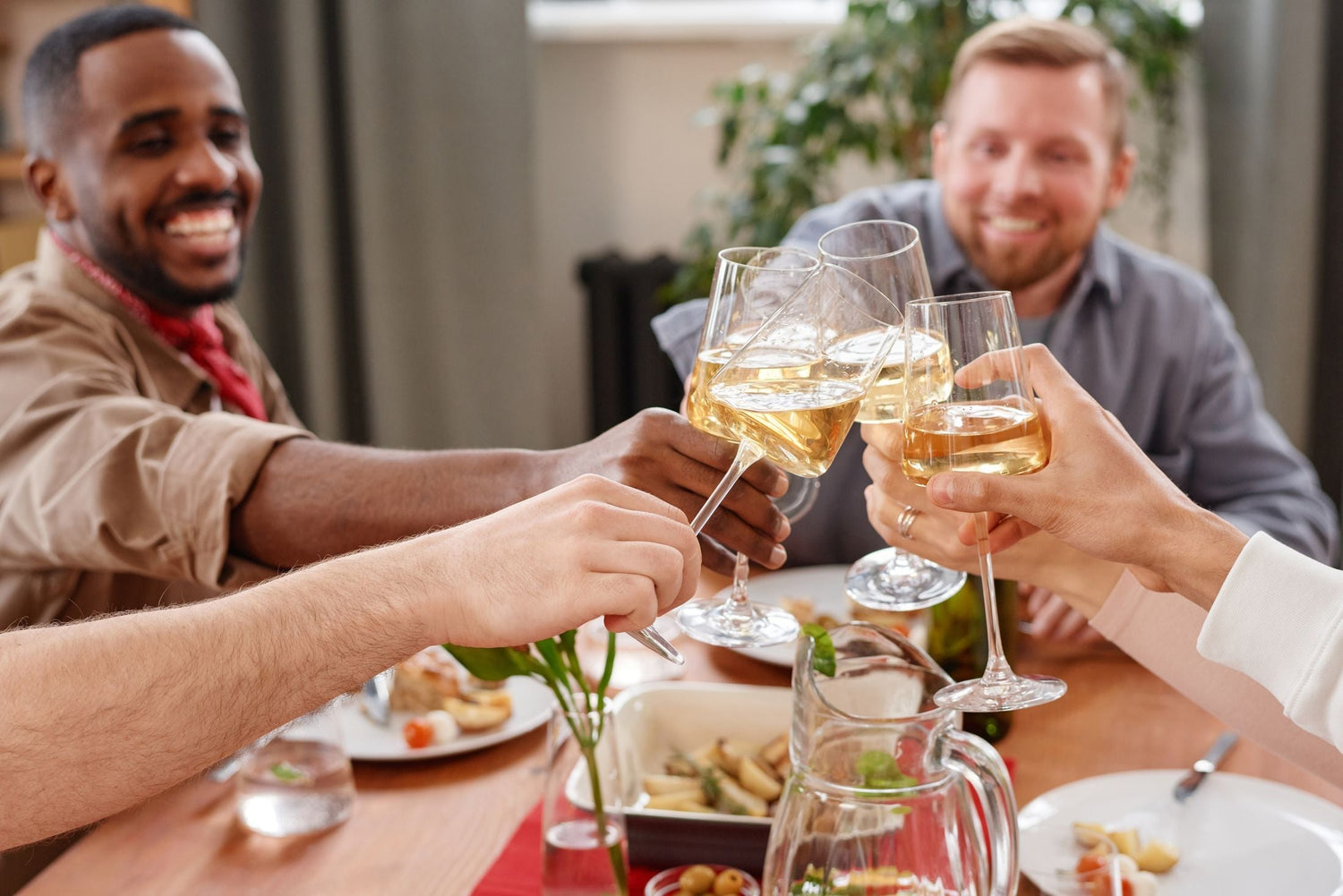 Friends clinking white wine glasses in a celebratory toast over a dinner table with food, perfect for marking special occasions