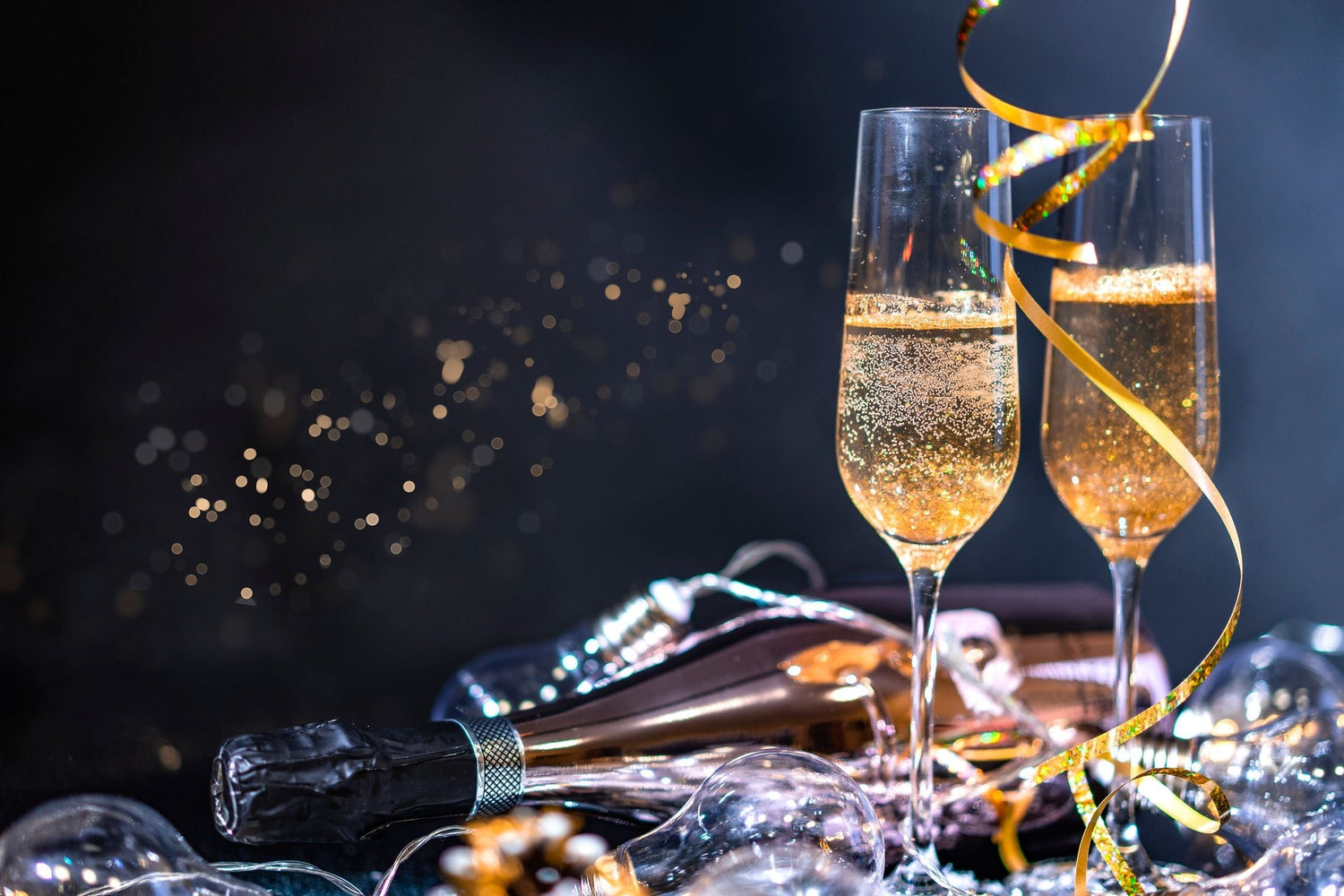 Two champagne flutes of sparkling wine with gold streamers and festive decorations against a dark background, celebration