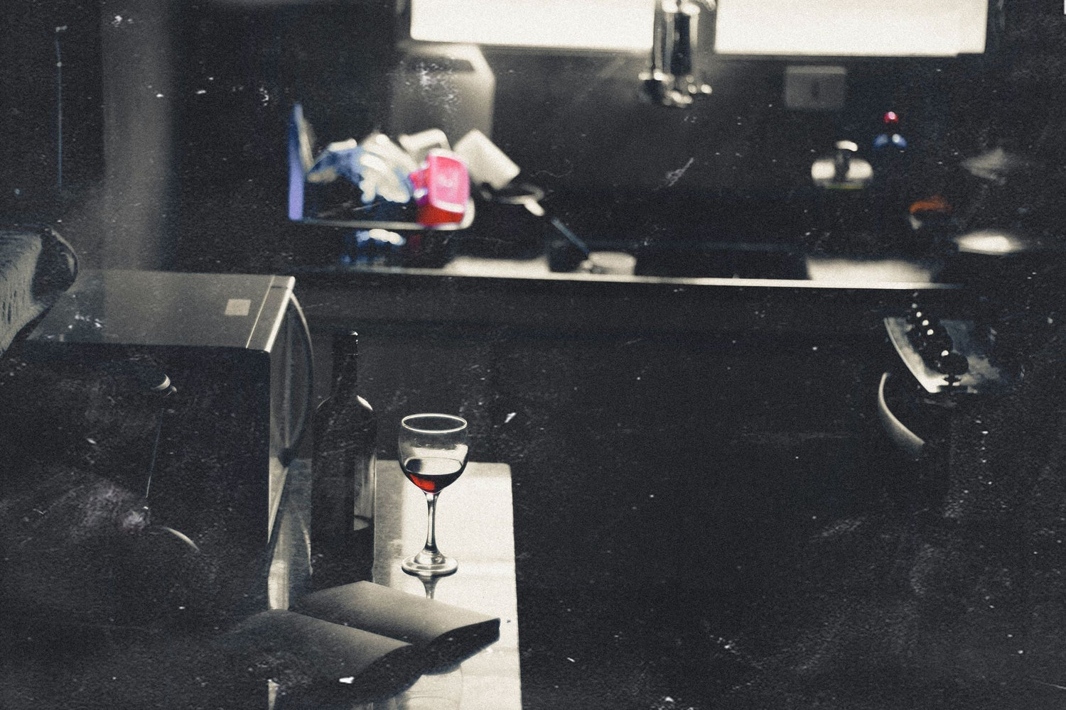A glass of red wine resting in low light beside a dark bottle, moody atmospheric styling for Red Orchid