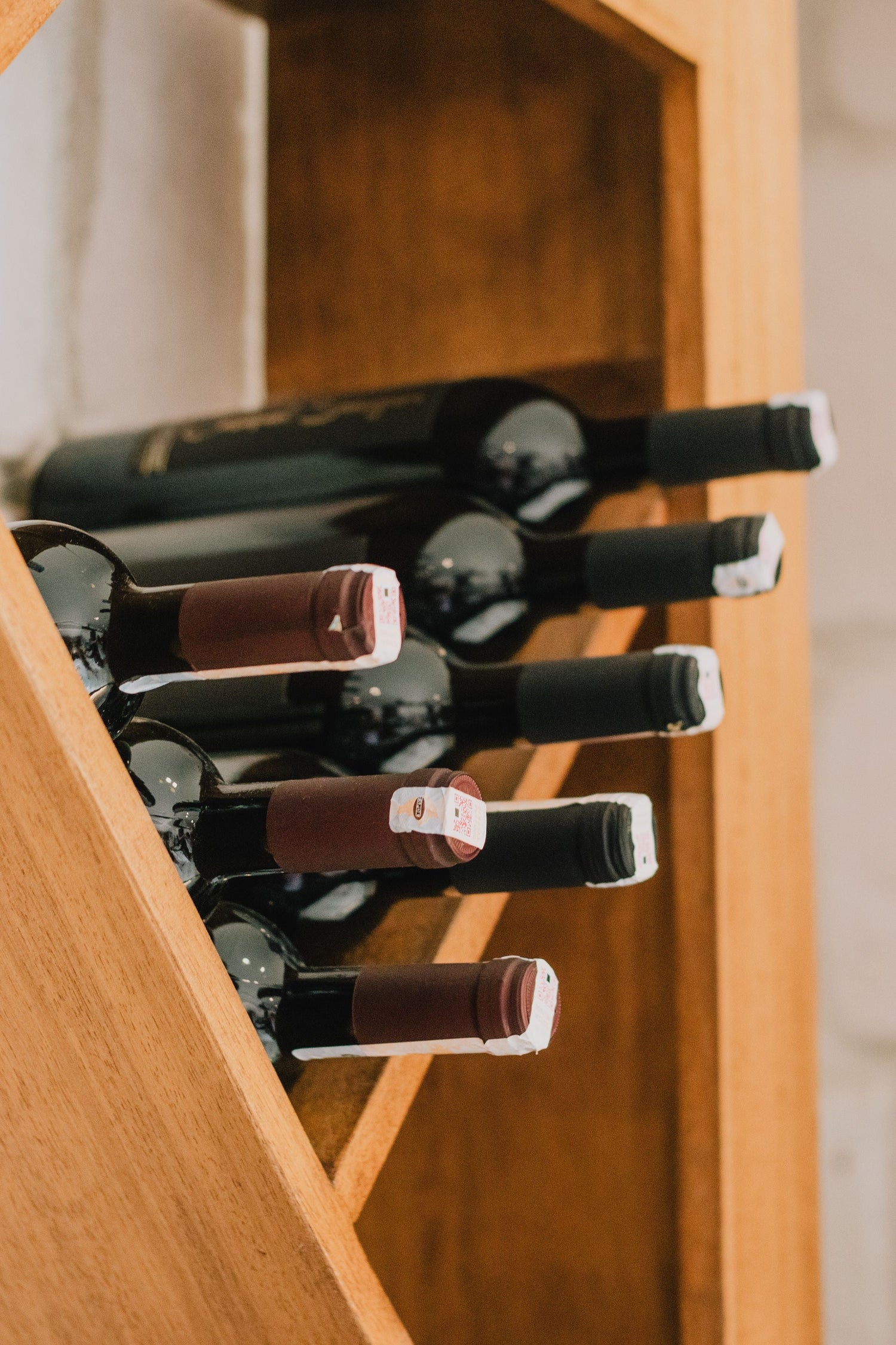 Red wine bottles stored in a honey-toned wooden wine rack, perfect for a mixed case selection