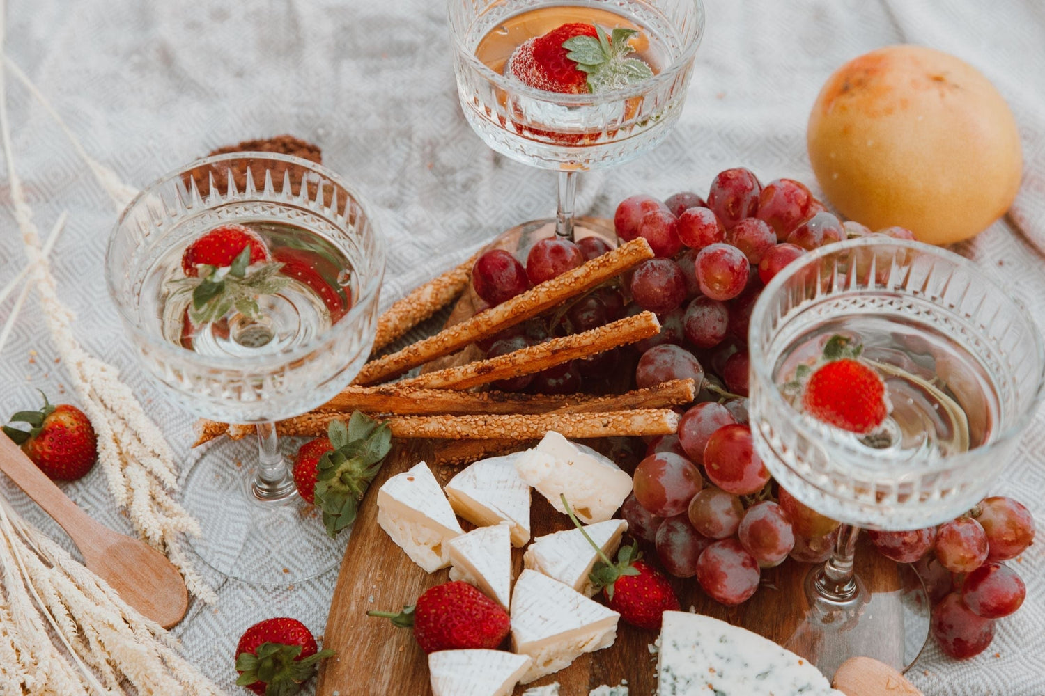 Crystal coupe glasses filled with dessert wine alongside fresh strawberries and a cheese board with grapes and crackers