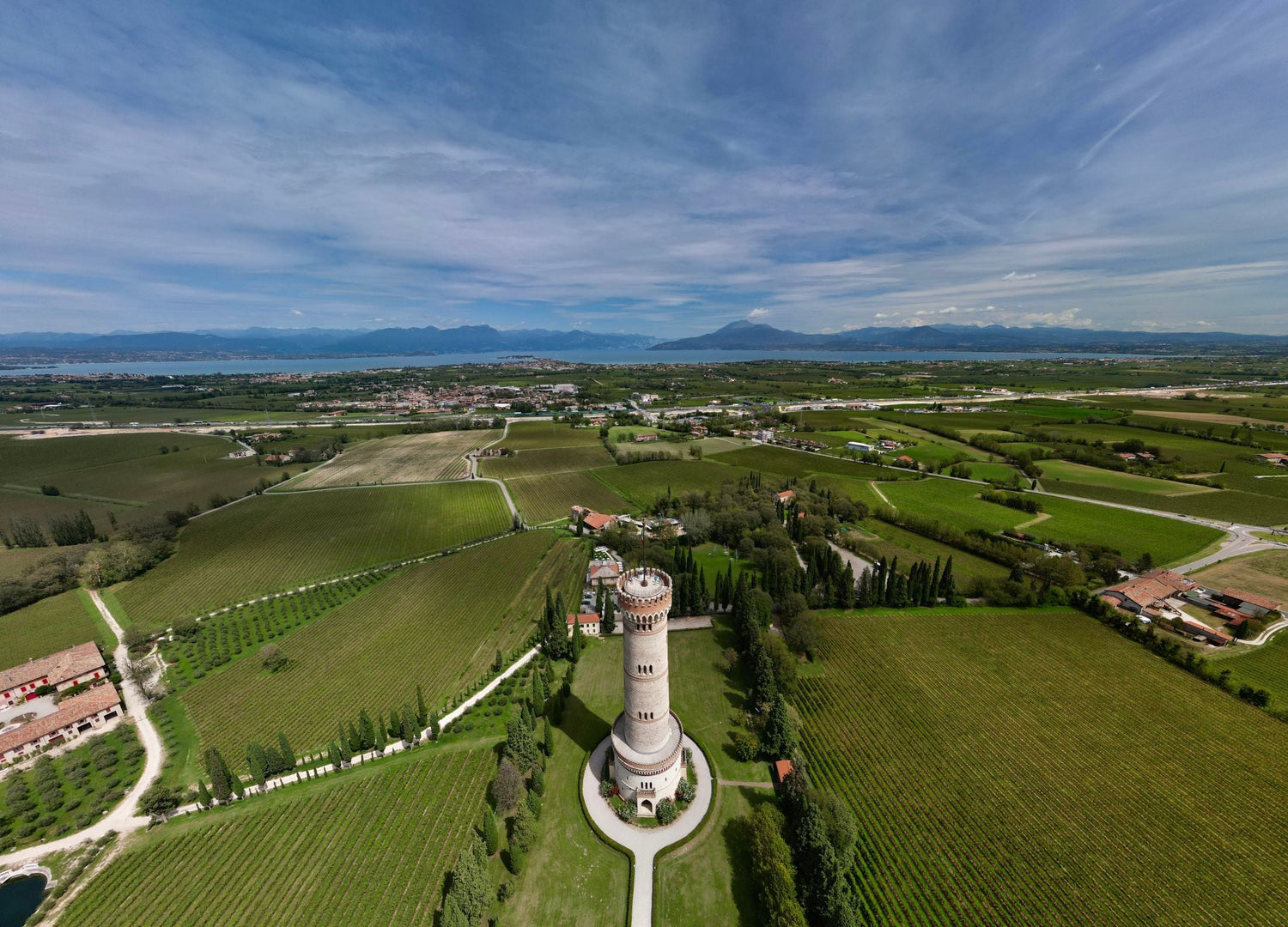 Aerial view of a medieval tower surrounded by vineyards with Lake Garda and the Alps visible behind, Lombardy, northern Italy