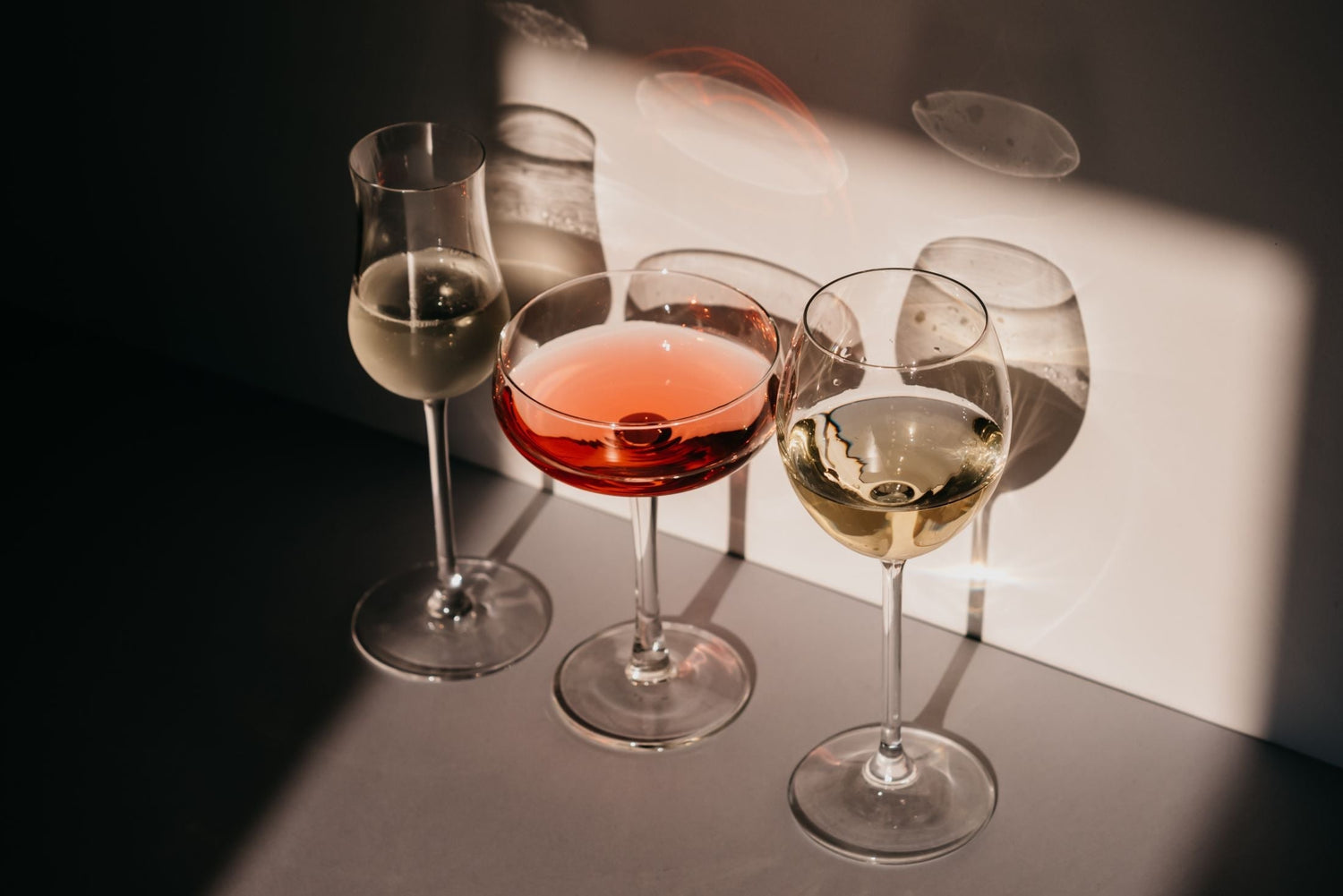 Three wine glasses — a champagne flute, a rosé coupe and a white wine glass — casting dramatic shadows in natural light, White Orchid