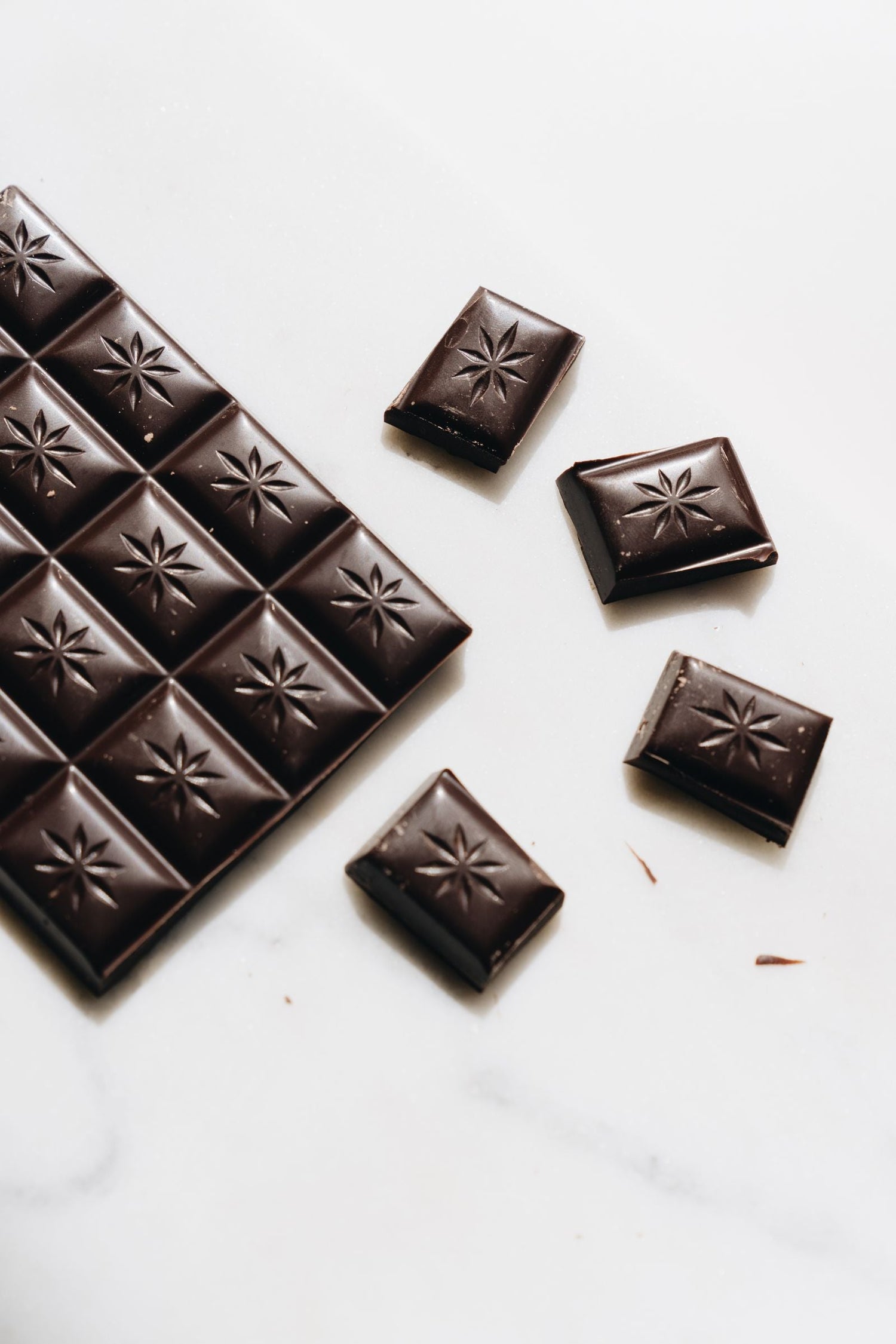Dark chocolate bar broken into individual squares scattered on white marble — wine pairing for chocolate desserts