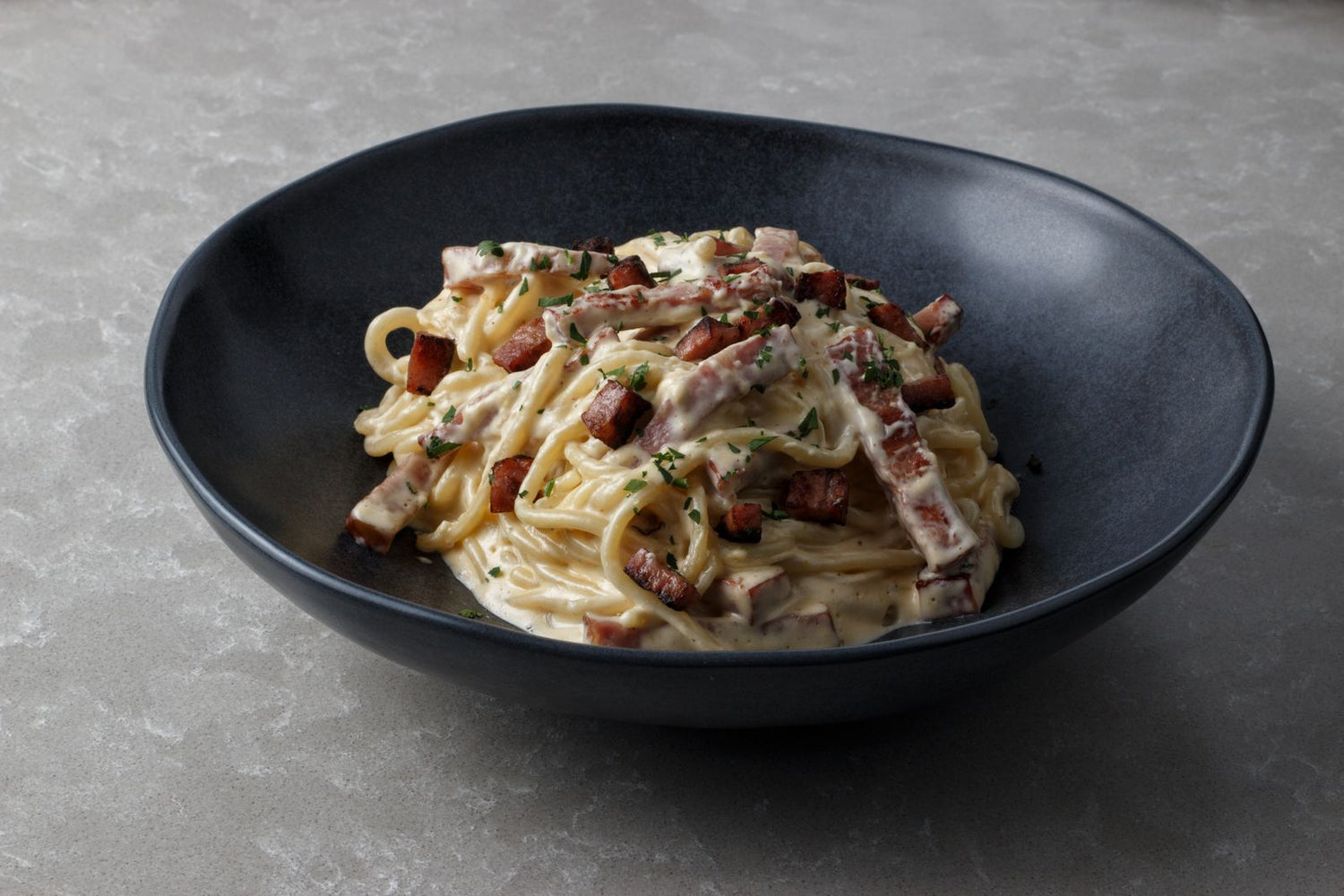 Spaghetti carbonara with rich cream sauce and crispy guanciale in a dark ceramic bowl — wine pairing for creamy pasta dishes