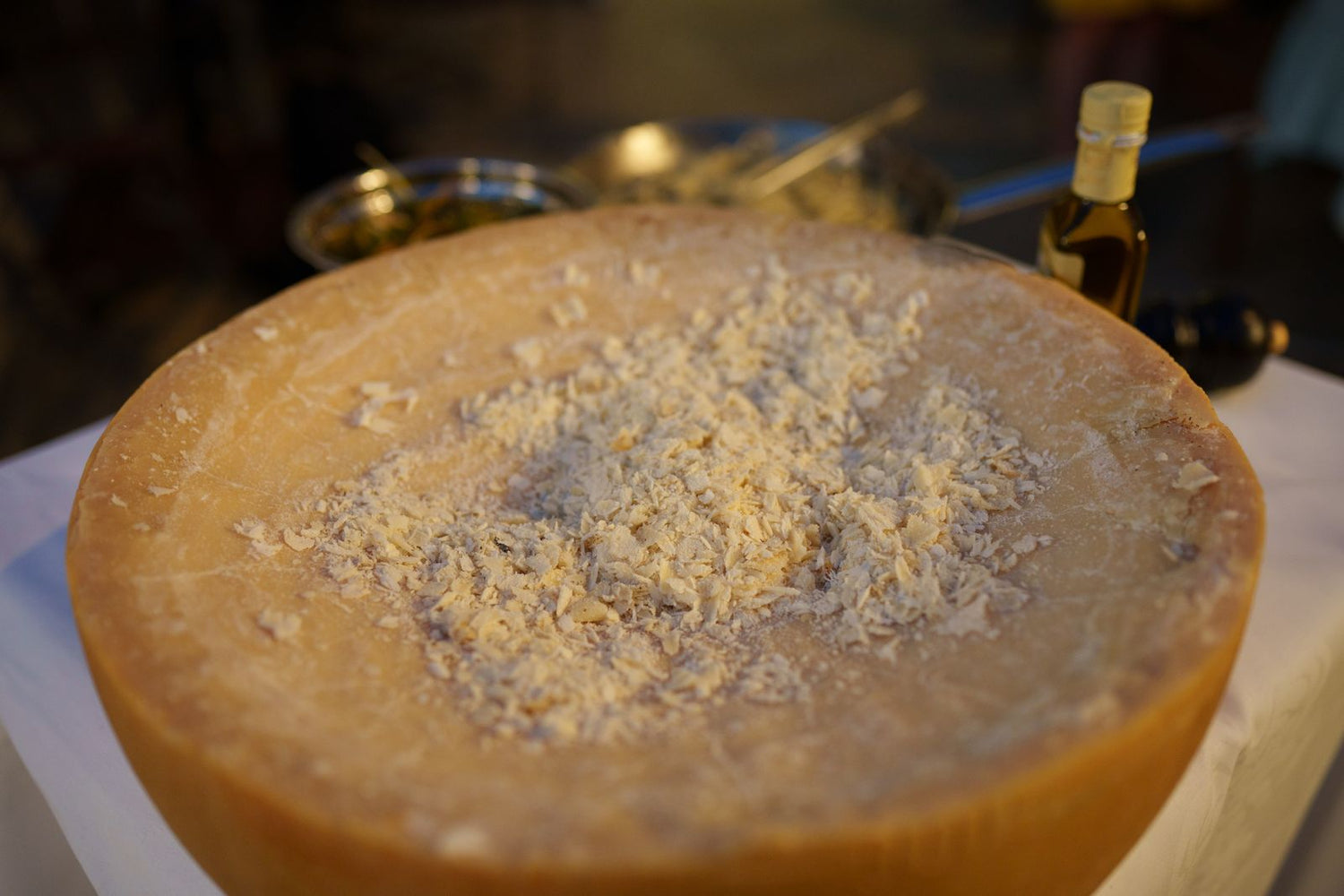A large wheel of aged Parmigiano-style hard cheese with freshly grated shavings scattered across the top — wine pairing for hard cheeses