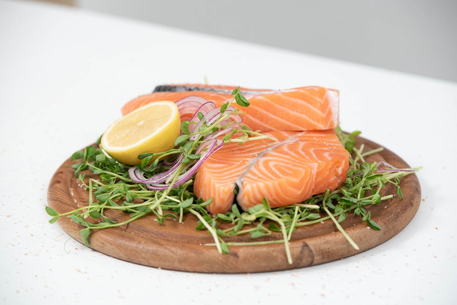 Two fresh salmon fillets on a wooden board with lemon, sliced red onion and microgreens — wine pairing for oily fish