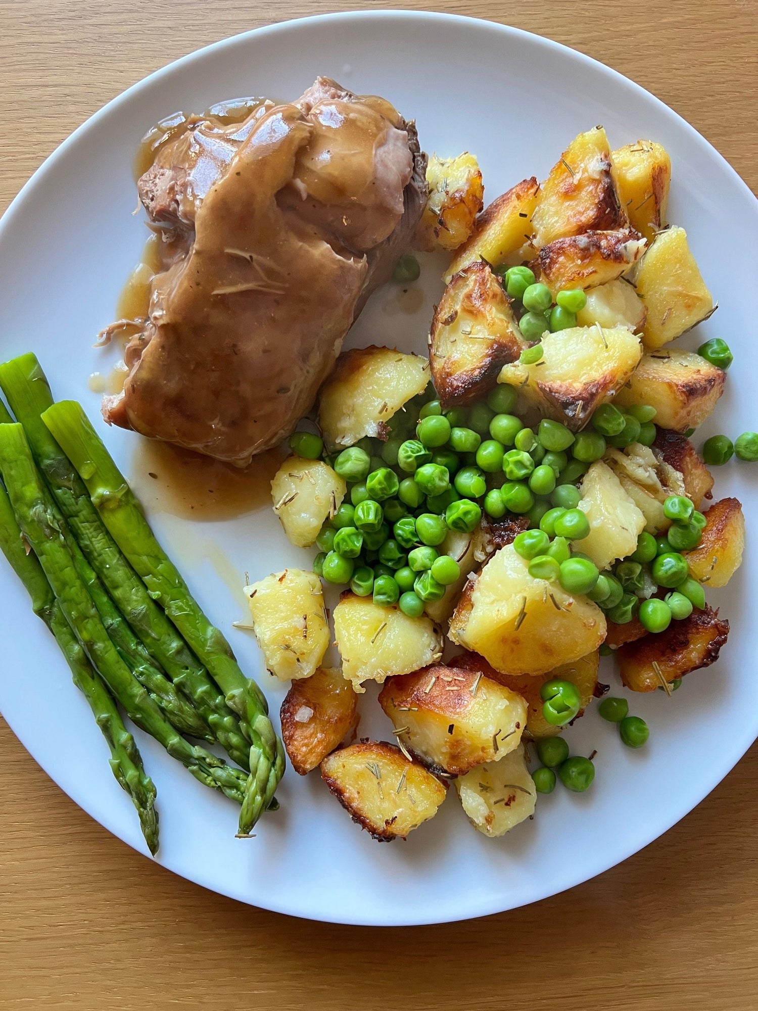 Roast pork with gravy, roasted potatoes, peas and asparagus.