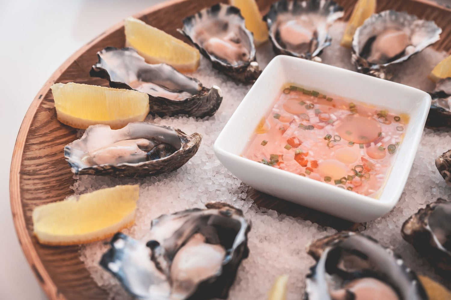 Freshly opened oysters on crushed rock salt with lemon wedges and a mignonette dipping sauce on a wooden board — wine pairing for shellfish