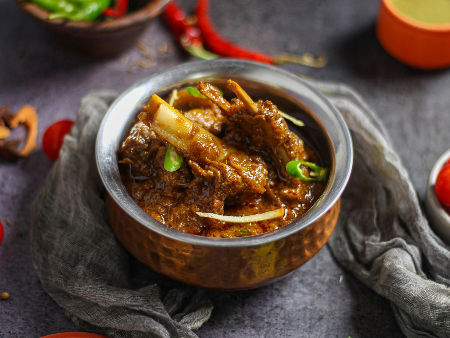 Rich dark spiced curry with bone-in meat in a hammered copper bowl, surrounded by red and green chillies — wine pairing for spicy food