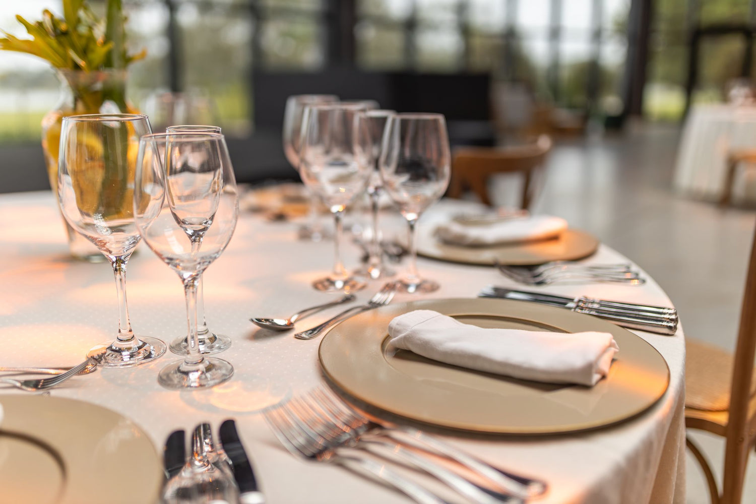 Long banquet table set with multiple empty wine glasses, gold charger plates and linen napkins at an elegant dining restaurant