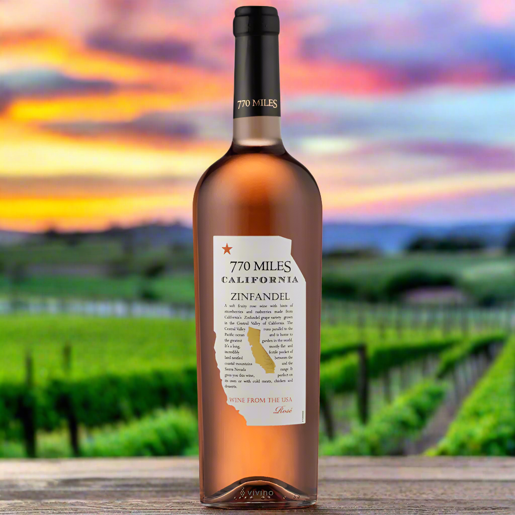 Place a bottle of 770 Miles White Zinfandel Rosé on a rustic wooden table with the warm glow of a California sunset over vineyard rows in the background.
