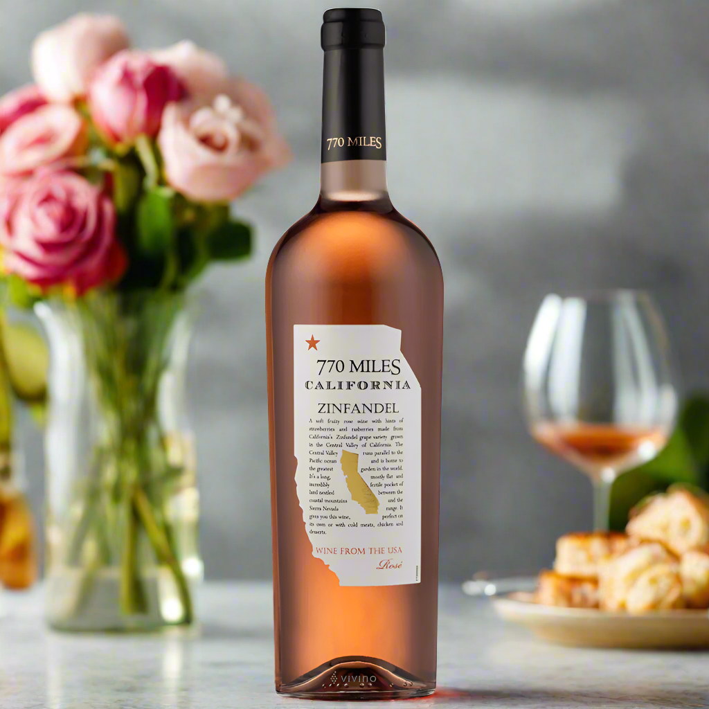 Place a bottle of 770 Miles White Zinfandel Rosé on an elegant garden table, surrounded by fresh flowers, soft lighting, and light summer dishes.