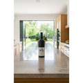 Babylonstoren Nebukadnesar wine bottle displayed on a natural-stone kitchen island in a bright contemporary home overlooking landscaped gardens.