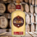 Cazcabel Tequila Reposado bottle displayed on a wooden barrel in a rustic tequila ageing room