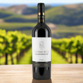 Bottle of Grand'Arte Alicante Bouschet wine on a wooden surface with a blurred vineyard background