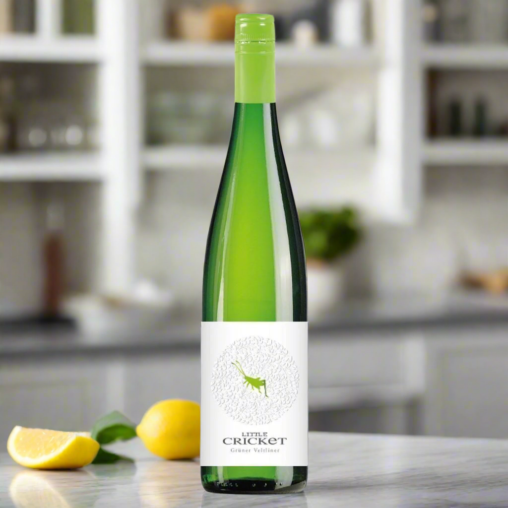 Place a bottle of Little Cricket Grüner Veltliner on a clean white kitchen counter with a bowl of lemons and a glass of wine, in soft natural light.