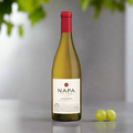 Napa Cellars Chardonnay bottle on a sleek white table with subtle reflections, paired with a clean backdrop of sunlit greenery or soft-focus grapes and citrus slices. Bright, elegant, and contemporary.