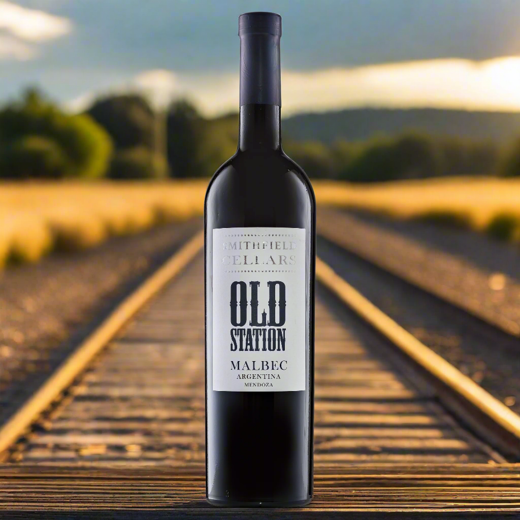 Old Station Malbec bottle on a barrel near railway tracks at golden hour