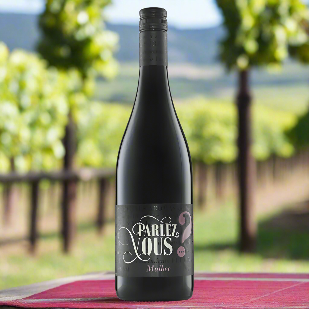 Parlez Vous Malbec bottle on a bistro table with vineyard in background