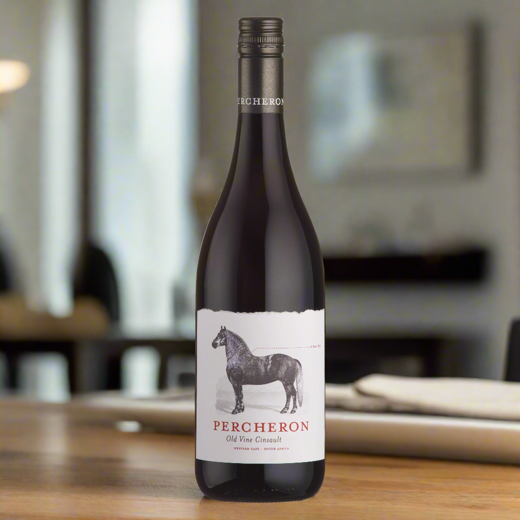 Place a bottle of Percheron Old Vine Cinsault on a modern dining table next to a glass of wine, with the backdrop of an elegant, softly lit dining room. The room features contemporary décor with warm lighting, creating an inviting and relaxed atmosphere.