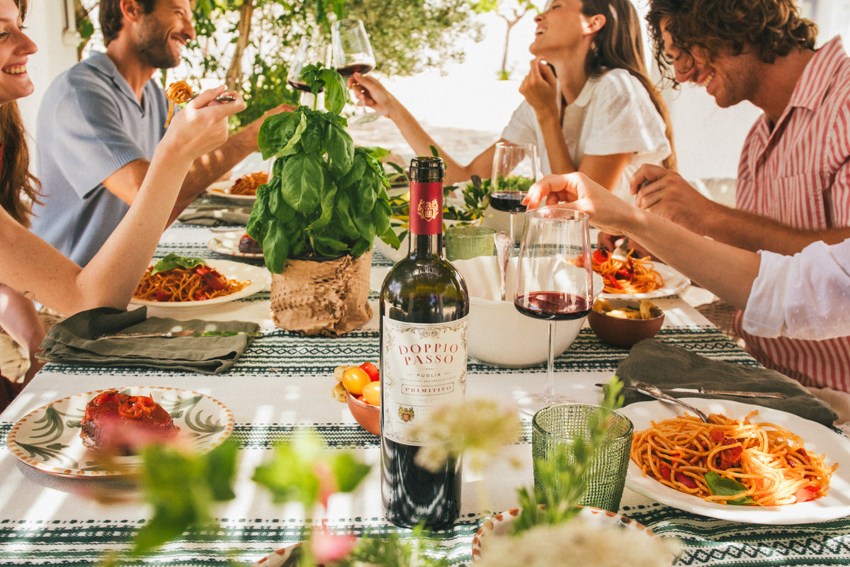 Group of people enjoying a meal outdoors with Doppio Passo Primitivo red wine and pasta.