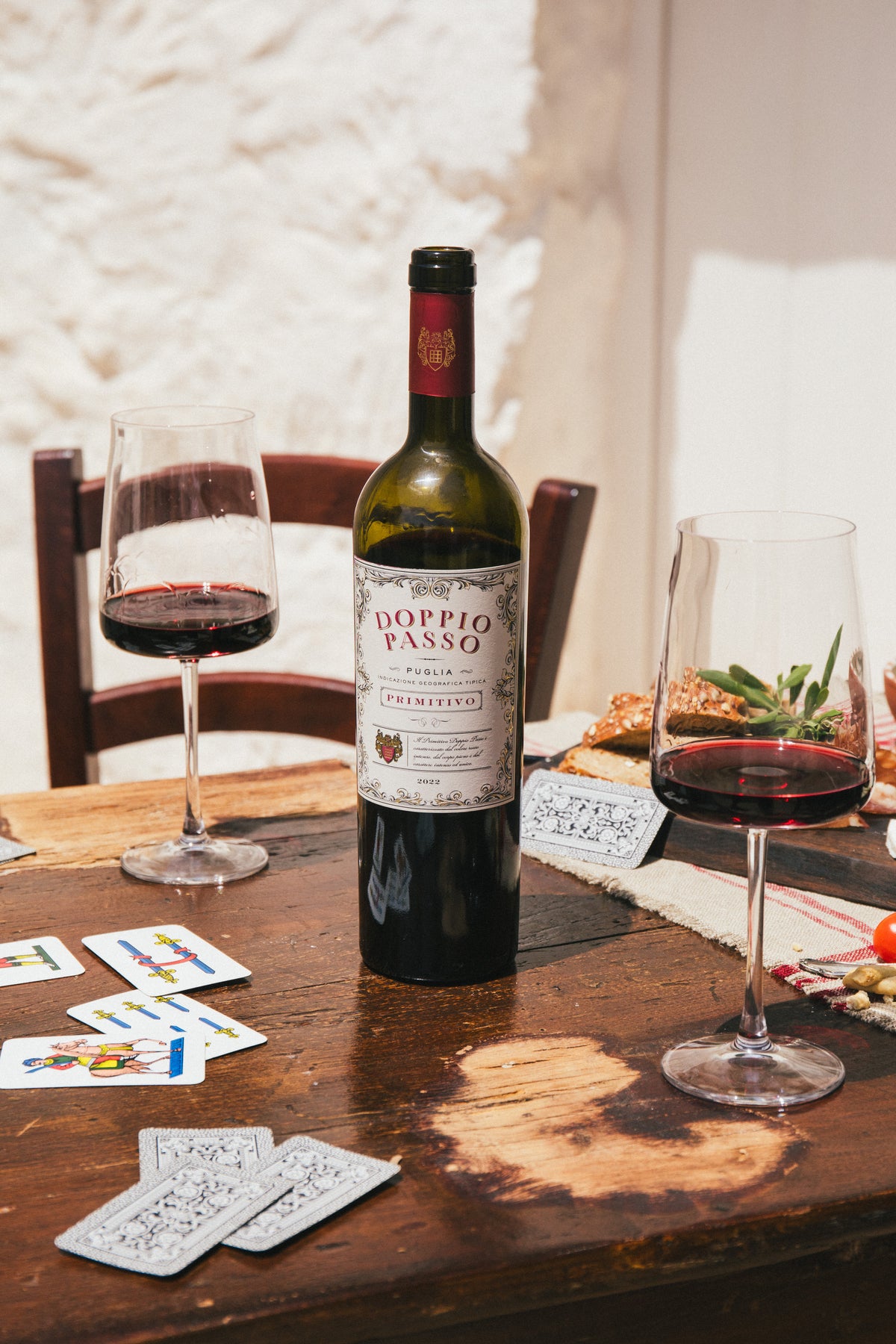 Bottle of Doppio Passio Primitivo red wine with two glasses on a table with cards and food.