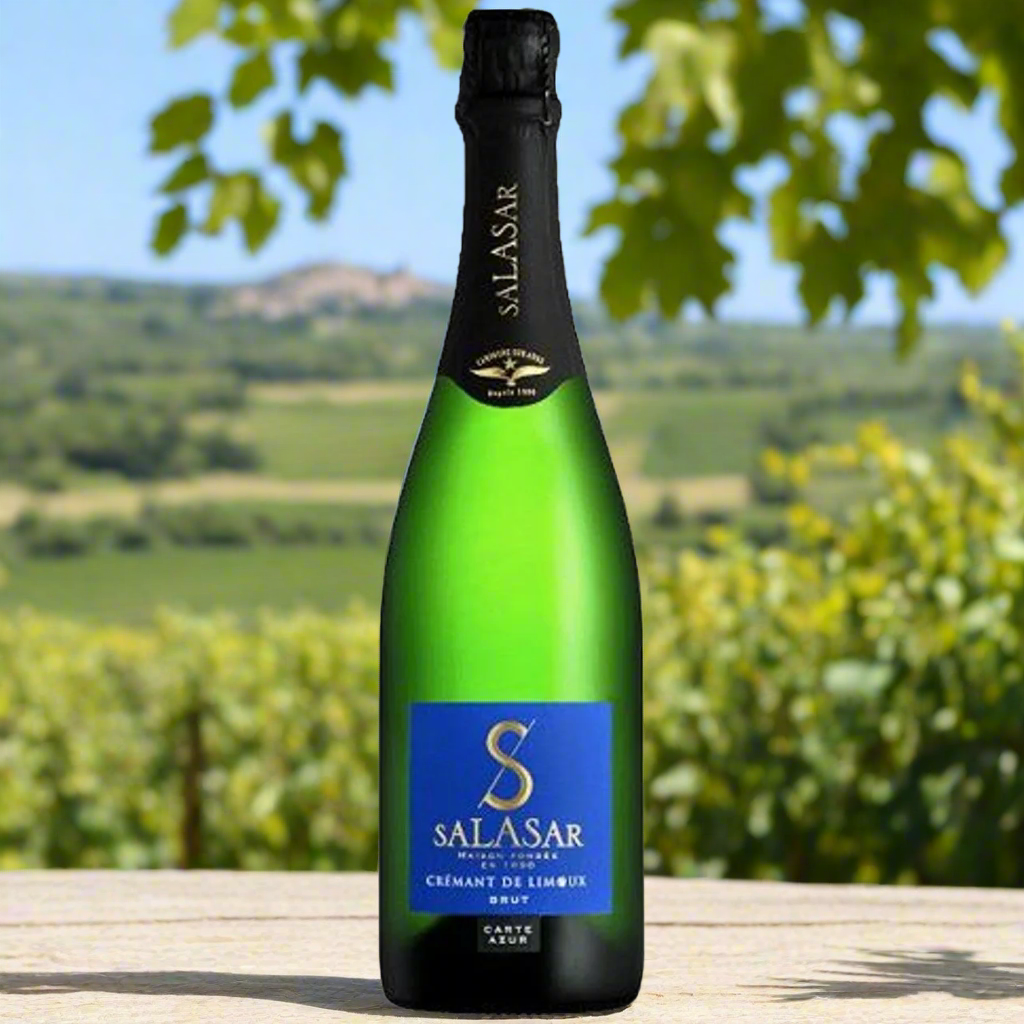 Limestone hillside vineyard in Limoux with panoramic views, a bottle of Crémant on a wrought iron table under a fig tree, surrounded by wildflowers and distant Pyrenees