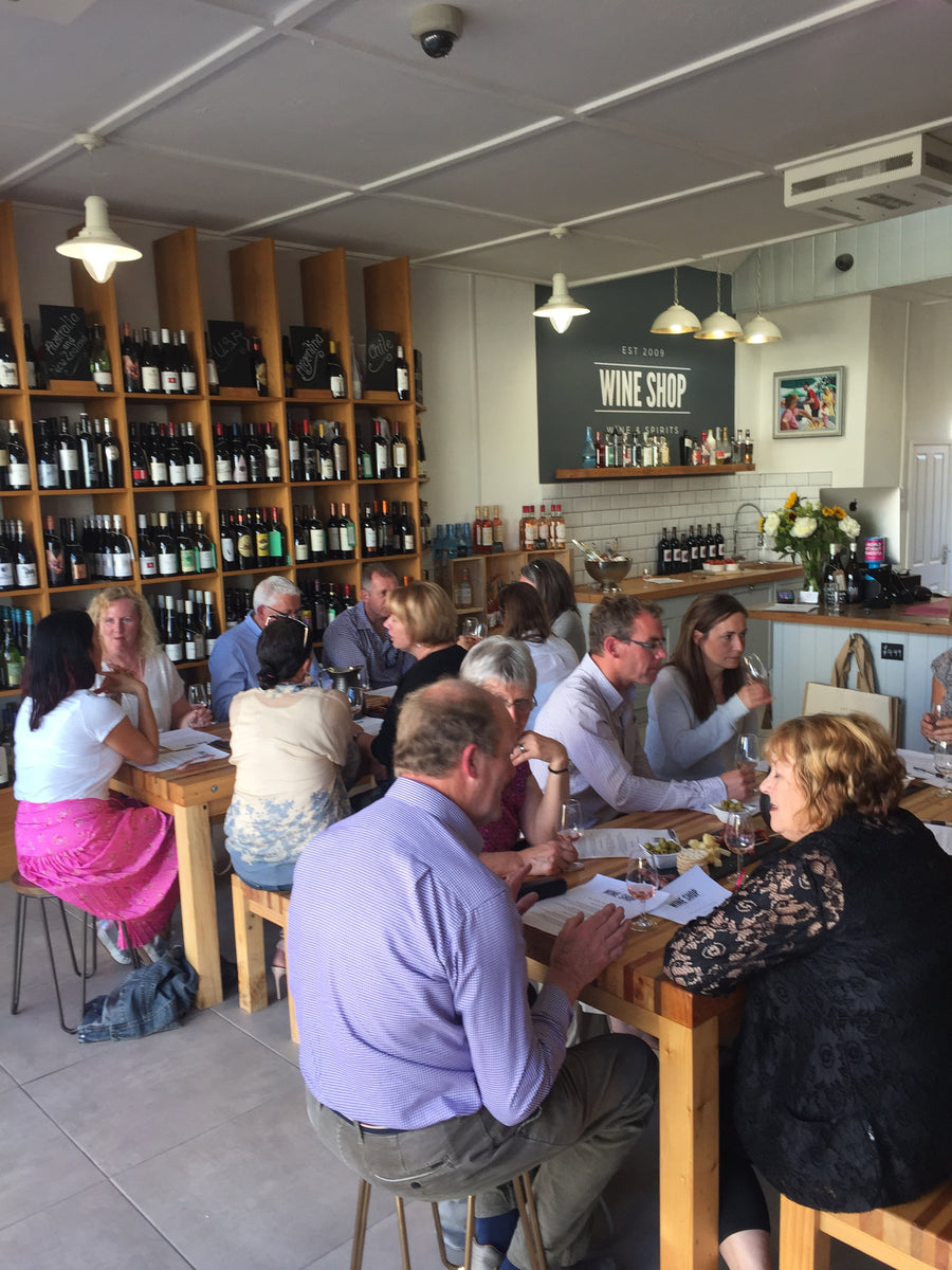 A busy tasting evening at The Wine Shop, Winscombe — customers around wooden tables with wine glasses